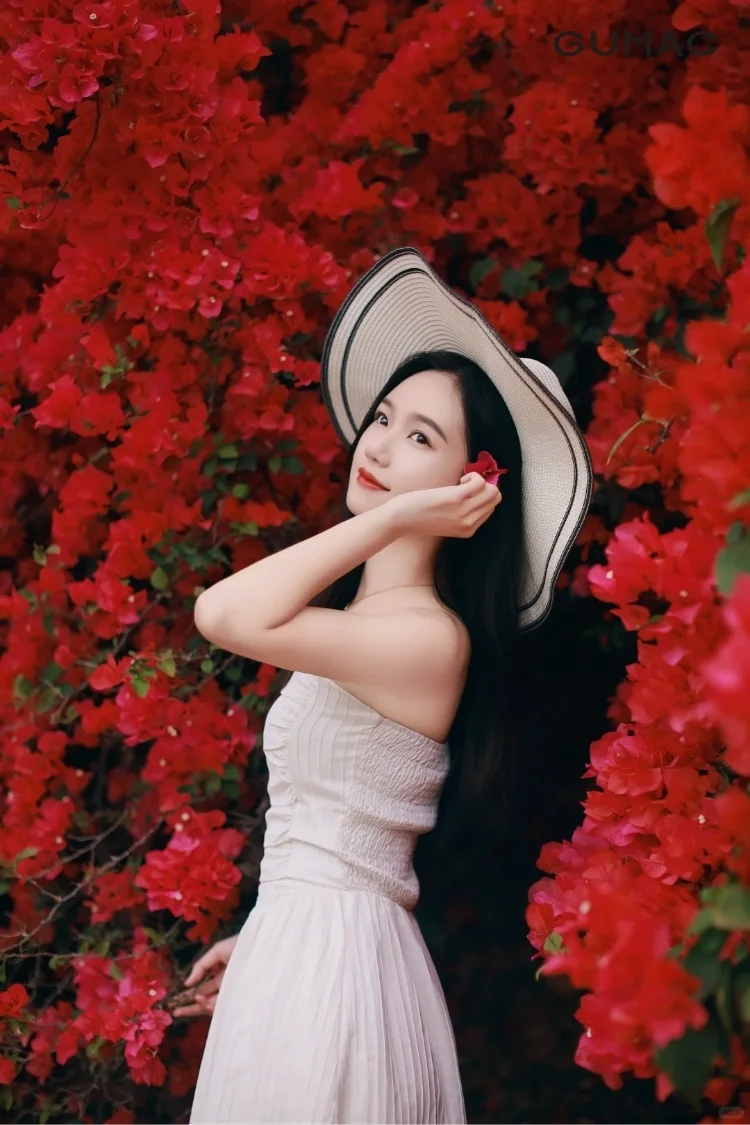 Người phụ nữ đội mũ tạo dáng trước bức tường hoa giấy đỏ