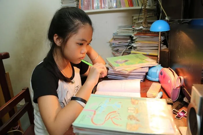 hình ảnh học tập bé gái chăm chú học bài tại bàn học đầy sách vở dưới ánh đèn bàn