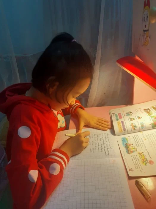 Bé gái học tập viết bài buổi tối dưới ánh đèn bàn đỏ