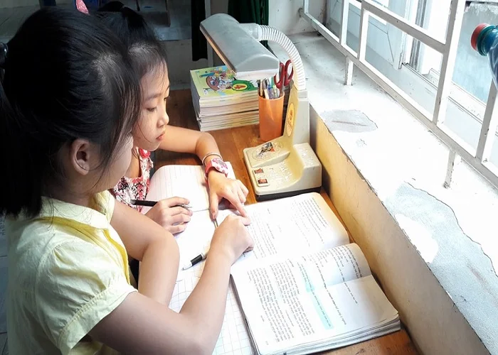 hình ảnh học tập chăm chỉ của hai bé gái cùng đọc sách bên bàn học cạnh cửa sổ